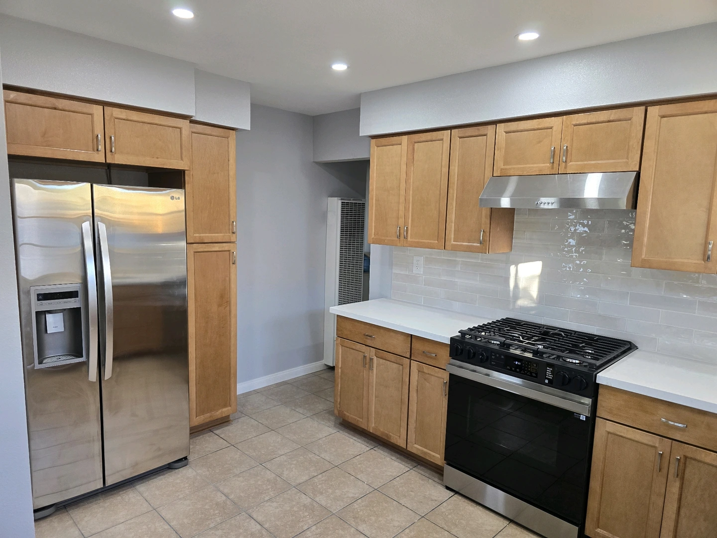 A kitchen with light brown wood cabinets and a stainless steel refrigerator and stove against light gray walls.